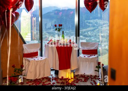 Dîner romantique de demande en mariage avec ballons en forme de cœur et vue sur les montagnes. Dîner romantique de demande en mariage avec ballons en forme de cœur, roses, bougies et décorations rouges Banque D'Images