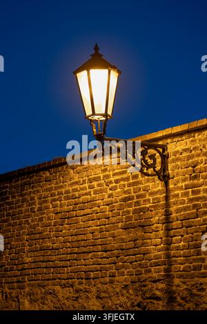 Lampe vintage la nuit fixée à et éclairant un mur de briques, source lumineuse unique contre un ciel bleu foncé à Vysehrad, Prague, Tchéquie. Banque D'Images