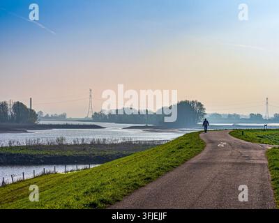 Person solitaire marchant sur un sentier le long d'un levée de rivière, profitant de la nature paisible et du paysage brumeux au printemps Banque D'Images