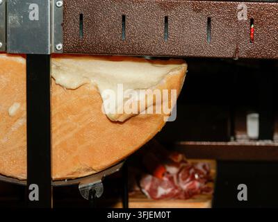Fromage fondant dans un grill raclette avec de la viande en arrière-plan Banque D'Images