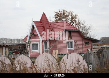 Une vue pittoresque d'une maison en bois de banlieue confortable avec une façade rose et un toit rouge abrupt derrière une clôture. Banque D'Images