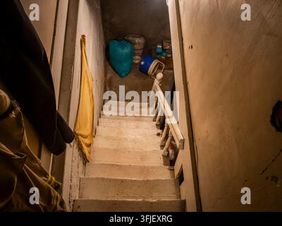 Regardant en bas des escaliers en bois abrupts menant à un espace de stockage sombre au sous-sol rempli d'anciens objets ménagers et de désordre Banque D'Images