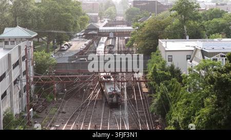 Train de banlieue approchant une gare historique du New Jersey, les câbles aériens croisent les voies alors que le quai se situe entre de vieux bâtiments en briques Banque D'Images