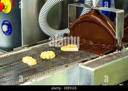 Procédé de glaçage des bonbons au massepain avec du chocolat sur une machine de tempérage du chocolat en usine Banque D'Images