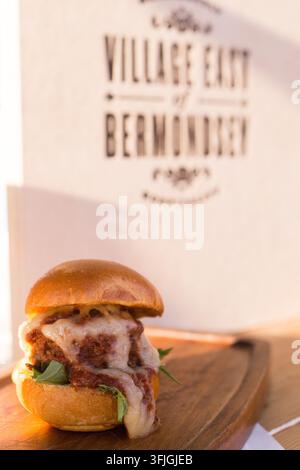 Un client savourant un slider au fromage et aux boulettes de viande servi sur une planche en bois Banque D'Images