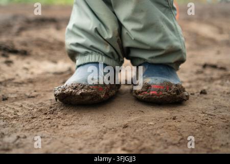 Un enfant joyeux et un tout-petit espiègle pataugent dans la boue épaisse, profitant d'un jeu en plein air insouciant dans la nature. Le garçon énergique éclabousse le sol mouillé avec une pure joie. Banque D'Images