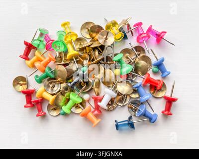 Pile de punaises à tête en plastique mélangées avec des têtes cylindriques coniques colorées & des punaises traditionnelles à tête plate en laiton....le tout sur un fond blanc. Banque D'Images