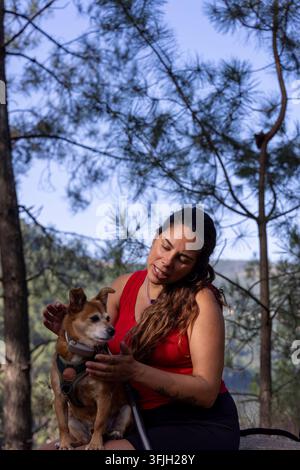 Femme hispanique enceinte aux longs cheveux caressant un petit chien en plein air, profitant de la nature et de la compagnie Banque D'Images