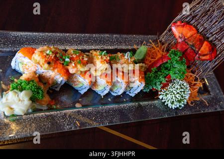 Une photographie élégante en contre-plongée mettant en valeur un rouleau de sushi spécial de qualité supérieure garni de morceaux de homard frits croustillants et d'orange vif masago, élaboré Banque D'Images