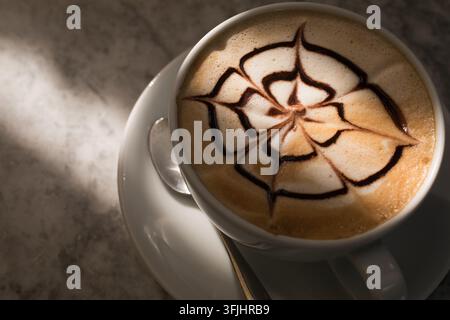 Dans un café ensoleillé, un barista prépare un cappuccino avec un art chocolaté complexe pour ravir un client avec du café artisanal. Banque D'Images