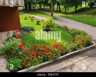 Une scène de jardin bien entretenue mettant en vedette des parterres de fleurs éclatants avec des soucis orange, rouges, roses et jaunes ainsi que d'autres fleurs colorées disposées le long d'un Banque D'Images
