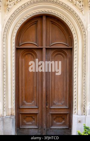 Une double porte en bois ornée se dresse dans une arche en pierre sculptée sur la façade d'un bâtiment. Banque D'Images
