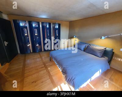 Intérieur de chambre moderne avec un grand lit doté de draps et de coussins bleu-gris posés contre un mur beige chaud. La pièce est en bois poli Banque D'Images