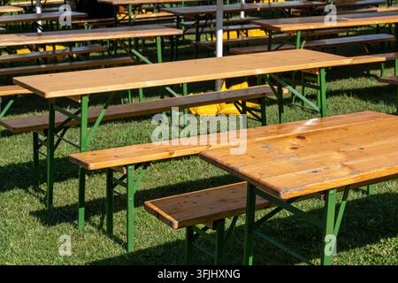 Des tables de pique-nique en bois vides se dressent sur l'herbe dans un lieu extérieur ensoleillé. Banque D'Images