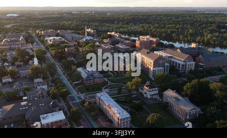 Voiture roulant le long d'une rue bordée d'arbres à travers le campus de l'Université Rutgers à New Brunswick, New Jersey, la rivière Raritan serpente devant des bâtiments en briques rouges et de Banque D'Images