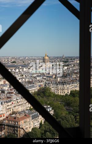 Un visiteur capture Paris à travers la Tour Eiffel, immortalisant la coupole dorée des Invalides pour documenter le paysage urbain emblématique. Banque D'Images