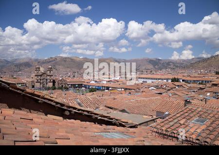 Vue en hauteur sur la ville montrant la mer de toits traditionnels en tuiles rouges sous un ciel bleu éclatant parsemé de nuages, entourée par les montagnes andines à Cusco Banque D'Images
