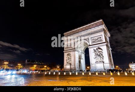 Vue en contre-plongé nocturne de l'arc de triomphe illuminé avec pavés de rue et ciel nocturne à Paris, France. Banque D'Images