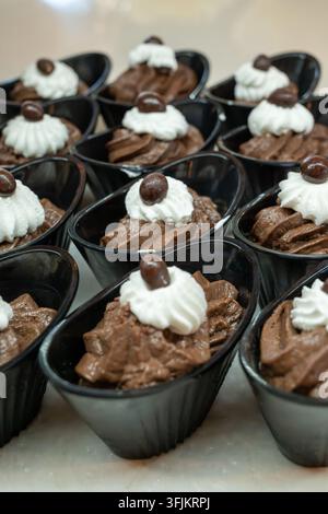 Tasses de mousse au chocolat avec crème fouettée et garniture au chocolat. Tasses noires disposées soigneusement pour le service. Parfaites pour les menus de desserts ou les événements de fête. Banque D'Images