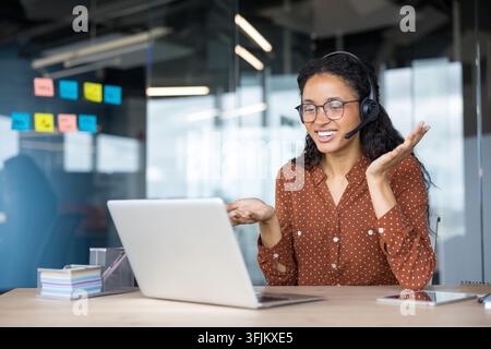 Support client et travail à distance, femme souriante avec casque utilisant un ordinateur portable pour un appel vidéo au bureau afin de discuter de la stratégie commerciale et de la communication avec les collègues lors d'une réunion professionnelle. Banque D'Images