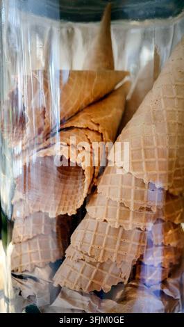 Cones de glace gaufrés croustillants vides empilés dans un bocal en verre transparent. Cônes de gaufres dorés au four prêts à servir du gelato ou des desserts d'été sucrés. Banque D'Images