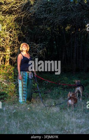 Femme enceinte souriant en promenant ses chiens le long d'un sentier forestier, incarnant la santé, le bien-être et un lien avec la nature Banque D'Images