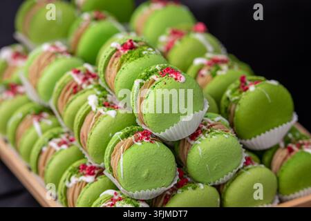 Gros plan de macarons à la pistache verte remplis de crème et décorés de baies séchées et de noix. Élégant dessert français aux couleurs vives Banque D'Images