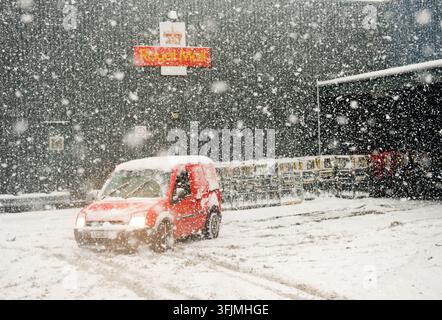 Un camion de livraison Royal Mail rouge roulant dans une forte chute de neige hivernale devant un dépôt Royal Mail. Banque D'Images