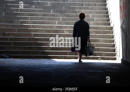 Silhouette d'une femme portant un sac à main montant des marches en béton dans un passage souterrain Banque D'Images