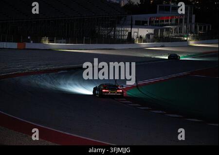 Voitures de course sportives roulant sur une section sombre de la piste avec les phares allumés lors d'une compétition d'endurance nocturne. Banque D'Images