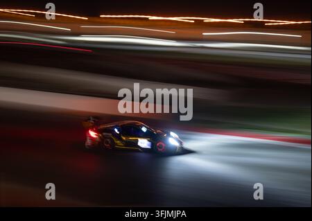 Plan panoramique abstrait d'une voiture de sport filant sur une piste de course la nuit avec des disques de frein lumineux et des traînées de lumière des phares brillantes. Banque D'Images