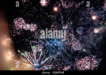 De nombreux feux d'artifice éclatent dans un ciel nocturne sombre en explosions superposées, remplissant l'air de fumée et d'étincelles colorées. Banque D'Images