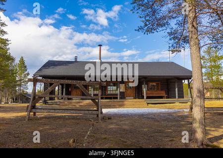 Laponie, Finlande - 18 mai 2026 : Une cabane en rondins traditionnelle dans le parc national Urho Kekkonen entourée de pins sous un ciel partiellement nuageux avec quelques Banque D'Images