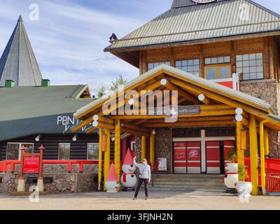 Rovaniemi, Finlande - 15 mai 2026 : Un touriste se tient les bras ouverts devant le bâtiment principal du bureau du Père Noël dans le célèbre Village du Père Noël lo Banque D'Images