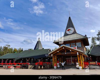Rovaniemi, Finlande - 15 mai 2026 : Un touriste se tient les bras ouverts devant le bâtiment principal du bureau du Père Noël dans le célèbre Village du Père Noël lo Banque D'Images