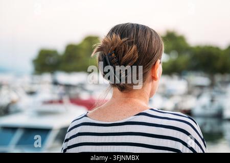 Vue arrière d'une femme regardant les bateaux amarrés dans un port de marina côtier à l'aube. Mise au point sélective. Banque D'Images