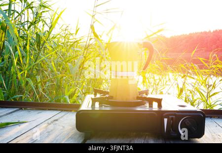 Préparation du café sur un brûleur à gaz portable de camping au coucher du soleil. Faire bouillir du café à l'extérieur sur une cuisinière à gaz au bord du lac au lever du soleil. Machine à expresso. Moka Pot sur portable Banque D'Images