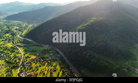 Une rivière sinueuse longe le pied d'une pente imposante alors que le soleil de l'après-midi inonde la vallée. Les champs et forêts des villages brillent de couleurs fraîches tandis que bleu r Banque D'Images