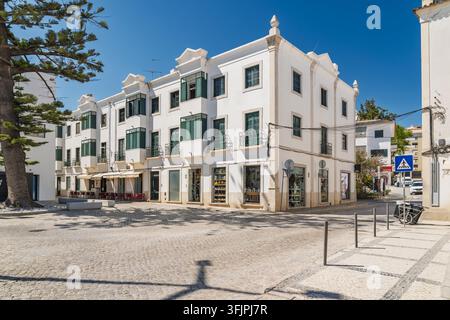 Vue d'un bâtiment traditionnel blanc avec des volets verts et des balcons sur une place pavée ensoleillée à Tavira, district de Faro, Portugal. Banque D'Images