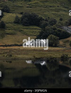 Vue d'une maison traditionnelle en pierre blanche nichée dans les collines verdoyantes avec un lac calme reflétant le bâtiment et le paysage environnant à Little Lang Banque D'Images