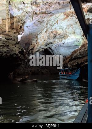 PHONG NHA, VIETNAM - 18 MARS 2026 : Bateau touristique bleu marqué PHONG NHA CAVE naviguant à travers la caverne brillamment éclairée remplie de stalactites suspendues Banque D'Images