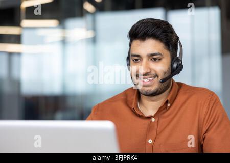 Représentant du service client travaillant sur un ordinateur portable, homme souriant avec casque fournissant une assistance à distance au bureau, concept de communication professionnelle et de service numérique pour les opérations commerciales. Banque D'Images