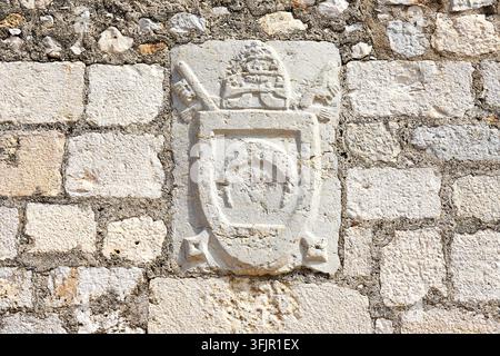 Un gros plan d'une gravure en relief sur pierre représentant les armoiries de la famille de Luna, encastrées dans un mur de pierre érodé. Le blason héraldique présente des détails complexes Banque D'Images