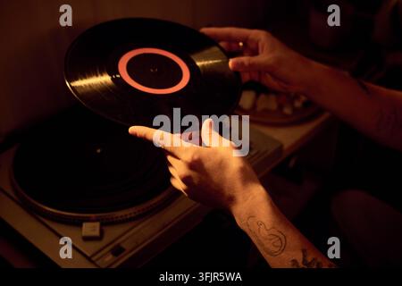 Mains d'un homme posant un vinyle sur un tourne-disque à la maison Banque D'Images