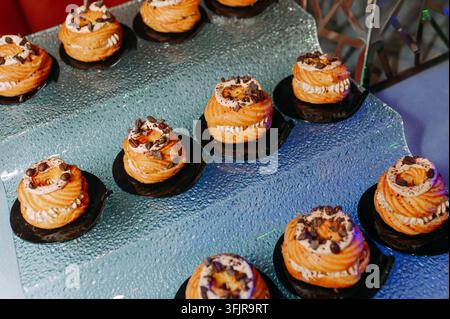Assortiment de choux fourrés à la crème avec garniture au chocolat sur des assiettes noires Banque D'Images
