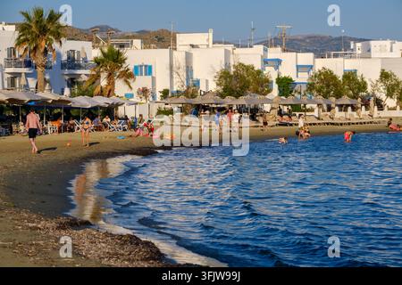 Naxos, Grèce – 1er juin 2026 : Baigneurs qui nagent et se font bronzer à la plage d’Agios Georgios avec des bâtiments en bord de mer et des palmiers Banque D'Images