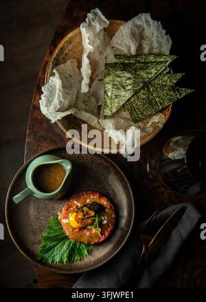 Vue aérienne d'une tartare de bœuf gastronomique avec jaune d'œuf, caviar et crackers de riz dans des assiettes en céramique. Banque D'Images
