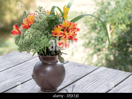 Bouquet de belles fleurs orange, rouge et jaune, Alstroemeria, lys péruvien, dans un vase sur une table dans le jardin Banque D'Images