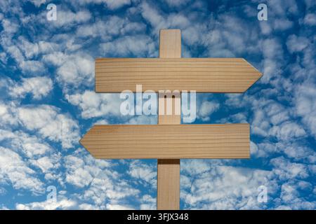 Panneau de signalisation en bois vierge contre un ciel bleu, gros plan. Panneau en bois vide avec deux flèches pointant dans des directions opposées contre un bleu éclatant Banque D'Images