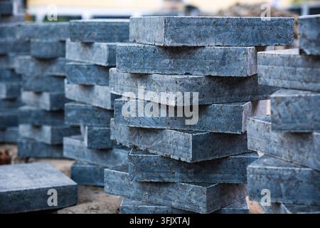 Vue rapprochée de plusieurs piles de dalles de pavage en granit gris foncé carrées et de blocs de béton prêts pour les travaux de construction de trottoirs en extérieur pendant Banque D'Images